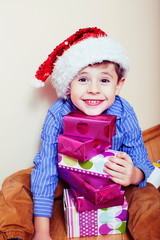 little cute boy with Christmas gifts at home wearing red Santas hat. closeup emotional happy smiling in mess with toys, lifestyle holiday people concept
