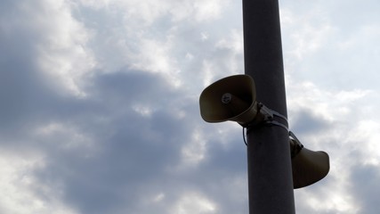 Two large megaphones mounted on a pole against a blue, slightly cloudy sky.