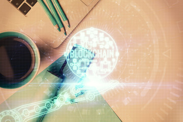 Blockchain theme hologram drawings over computer on the desktop background. Top view. Multi...