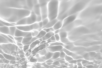 Blurred desaturated transparent clear calm water surface texture with splashes and bubbles. Trendy abstract nature background. White-grey water waves in sunlight.