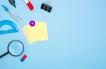 The concept of school and students. Empty square colored paper for writing in the middle. School and office stationery on the edges on a blue background. Top view, free space for text.