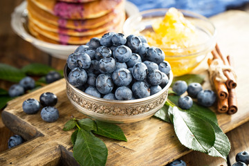Blueberries in a plate and pancakes, on an old background.