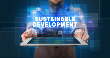 Young business person working on tablet and shows the inscription: SUSTAINABLE DEVELOPMENT