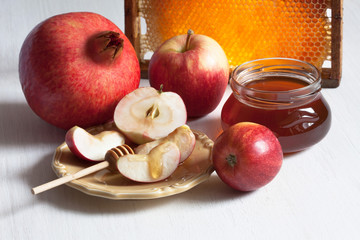 Rosh Hashanah holiday, greeting card, background with a jar of honey, pomegranate, apples, a plate with slices and honeycomb on a white wooden table.