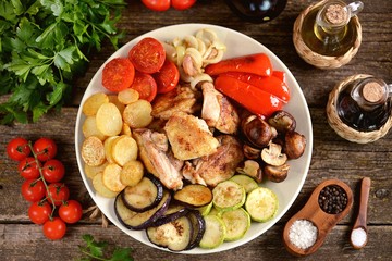 Fried chicken slices with potatoes,  bell peppers, eggplant, zucchini, cherry tomatoes, mushrooms and onions on a wooden background.
