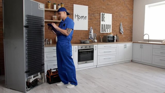 Worker repairing refrigerator in kitchen