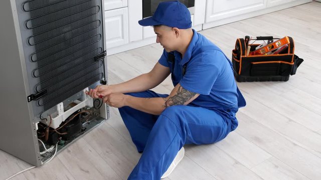 Worker repairing refrigerator in kitchen