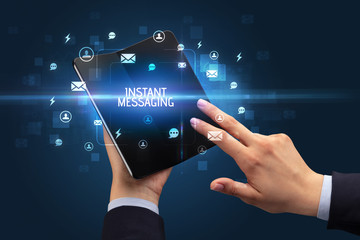 Businessman holding a foldable smartphone with INSTANT MESSAGING inscription, social networking concept