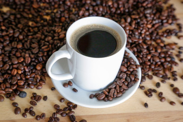  A cup of black coffee with coffee grains, natural light on wooden table