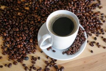  A cup of black coffee with coffee grains, natural light on wooden table