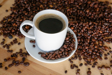  A cup of black coffee with coffee grains, natural light on wooden table