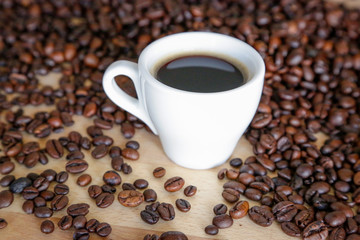 Coffee grains with white cup on coffee on wooden table, natural light