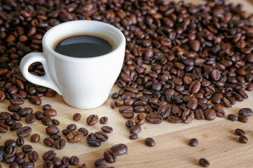 Coffee grains with white cup on coffee on wooden table, natural light