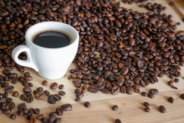 Coffee grains with white cup on coffee on wooden table, natural light