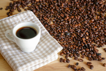 Coffee grains with white cup on coffee on wooden table, natural light