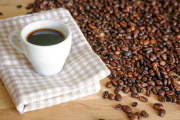 Coffee grains with white cup on coffee on wooden table, natural light