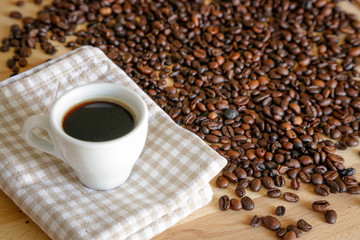 Coffee grains with white cup on coffee on wooden table, natural light