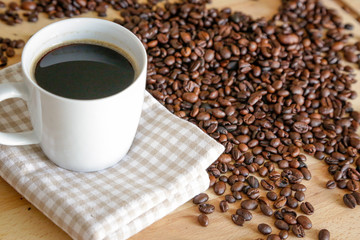 Coffee grains with white cup on coffee on wooden table, natural light