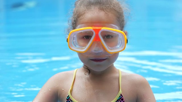 Portrait little girl in an underwater mask floating in an outdoor pool.Active rest in the water park. Happy Kid or Child preparing for diving.Girl in snorkel raising thumb doing ok sign before diving.