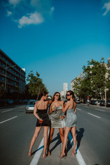 Three attractive caucasian women in summer tight dresses posing with cocktails on the road. Fashion and beauty	