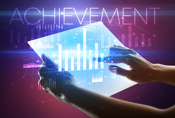 Hand holding futuristic tablet with ACHIEVEMENT inscription above, modern business concept