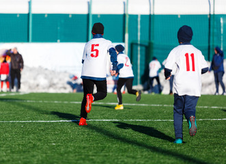 Obraz premium Boys in white red sportswear running on soccer field with snow on background. Young footballers dribble and kick football ball in game. Training, active lifestyle, sport, children winter activity 