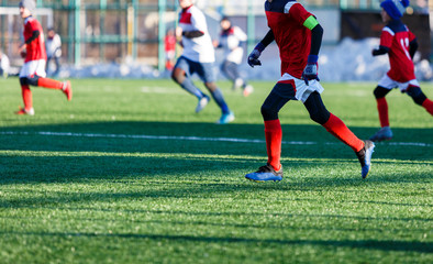 Boys in white red sportswear running on soccer field with snow on background. Young footballers dribble and kick football ball in game. Training, active lifestyle, sport, children winter activity 