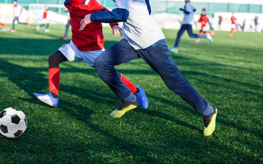 Boys in white red sportswear running on soccer field with snow on background. Young footballers dribble and kick football ball in game. Training, active lifestyle, sport, children winter activity 