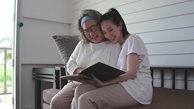 Smiling mother and daughter sitting on sofa reading book