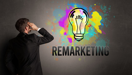 businessman drawing colorful light bulb with REMARKETING inscription on textured concrete wall, new business idea concept