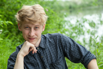 Closeup portrait of young blonde guy in blue shirt in autumn park