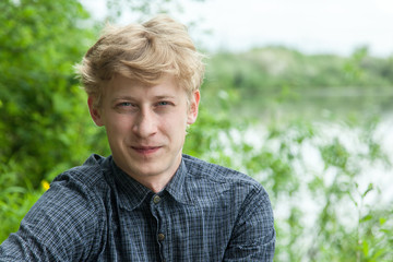 Closeup portrait of young blonde guy in blue shirt in autumn park