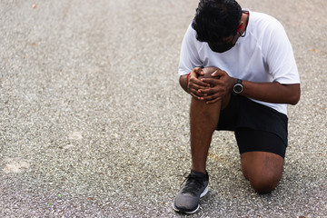 Close up Asian young sport runner black man wear watch sitting hands joint hold knee pain during...