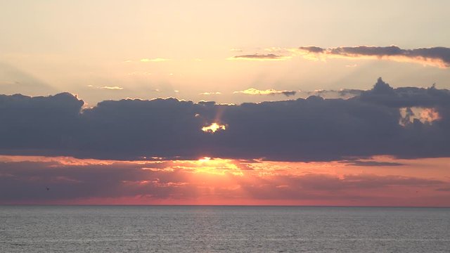 Golden sunset beaming through clouds sun rays pink purple yellow glimmer over waves wide static Lake Huron