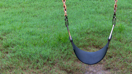 An empty  children swing hanging above a lush green grass carpet