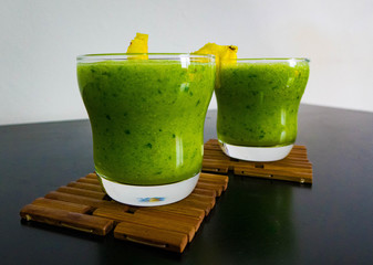 Healthy, natural and detoxifying green drink with pineapple in transparent glass on wooden coasters