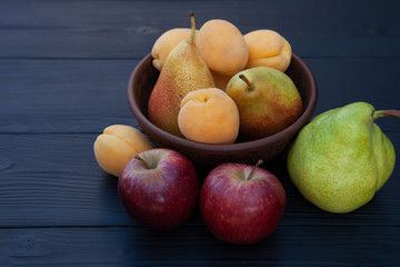 Apricots, pears and apples on a dark wooden background.