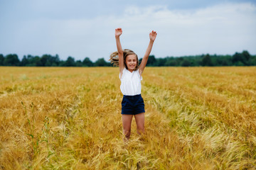 A happy and smiling girl jumps with her hands in the air in a wheat field