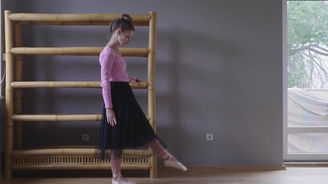 slender woman in pink sweater, black ballet skirt and pointe shoes doing exercises at home, adapting existing furniture for this