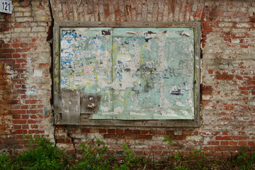 Old dirty wooden board with scraps of advertisements on a vintage red brick wall.