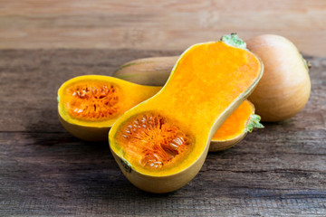 Butternut squash whole and sliced ​​on a wooden table. Butternut is a bell-shape fruit with sweet orange-yellow flesh.