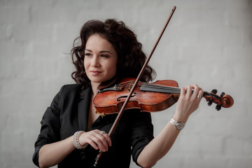 Young attractive brunette girl of Asian appearance on a white brick background with a violin in her hands.