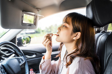Asian business woman beautiful pretty attractive driving in car vehicle doing makeup applying on lipstick chap stick looking into mirror, one-person parking getting ready in hurry fast lifestyle