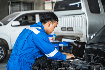 Mechanic Asian man using laptop computer examining tuning fixing repairing car engine automobile vehicle parts using tools equipment in workshop garage support and service in overall work uniform