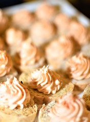 Cookies decorated with twirling creamy frosting on top served on a white plate at a cocktail party