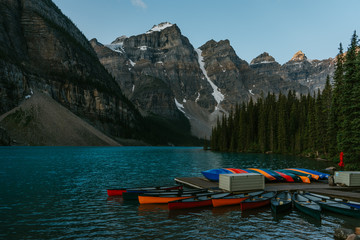 Colorful kayak boats on the beautiful iconic Moraine Lake in Canadian Rockies, Alberta, Canada. Sunrise mountain landscape on background.