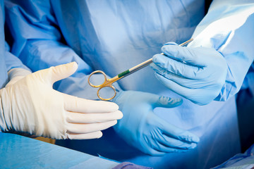 Close up of a hemastat being passed by two medical professionals in surgical setting