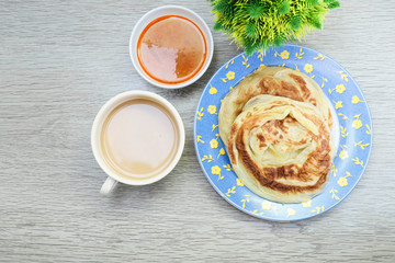 The famous Malaysian breakfast, Roti Canai on the plate with curry, and a cup of coffee