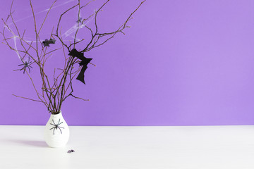 Halloween decorations, paper bats flying on tree branch and spiders on table over purple background.