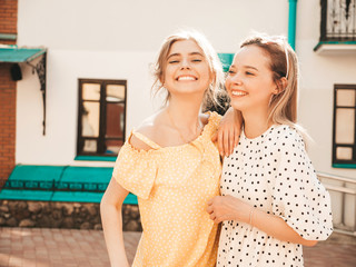 Two young beautiful smiling hipster girls in trendy summer sundress.Sexy carefree women posing on street background in sunglasses. Positive models having fun and hugging